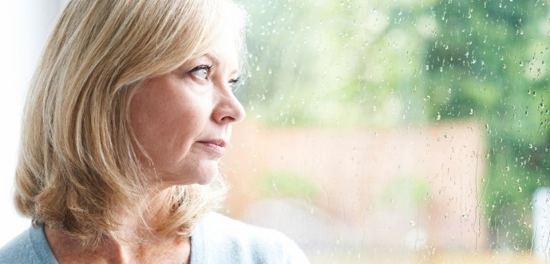 femme ayant pluys que la 50ène qui regarde par la fenetre avec un air triste